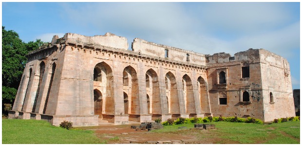 Hindola Mahal literally means a “Swinging Palace” a name given to its peculiar sloping sidewalls. The plan of the building is ‘T’ shaped, with a main hall and transverse projection to the northern side. The massive vaulted roof of the hall has disappeared though the row of lofty arches, which once supported it, is still intact. This large audience hall is dated to 15th century AD. Muk.khan CC BY 3.0