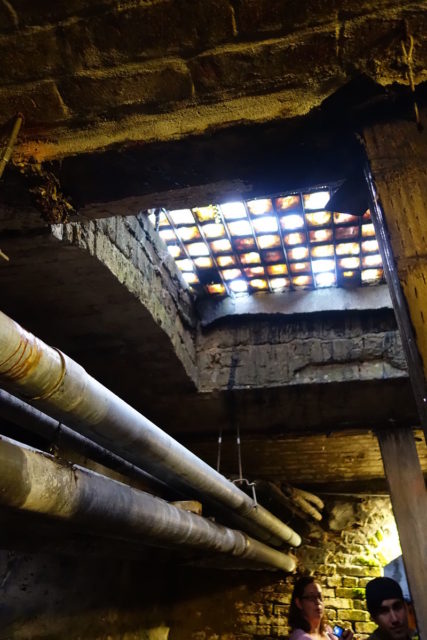 A view from the Seattle Underground looking upwards at the glass skywalks built above the previous street level which supports the current sidewalk. Author: Mark Hursh CC BY-SA 3.0