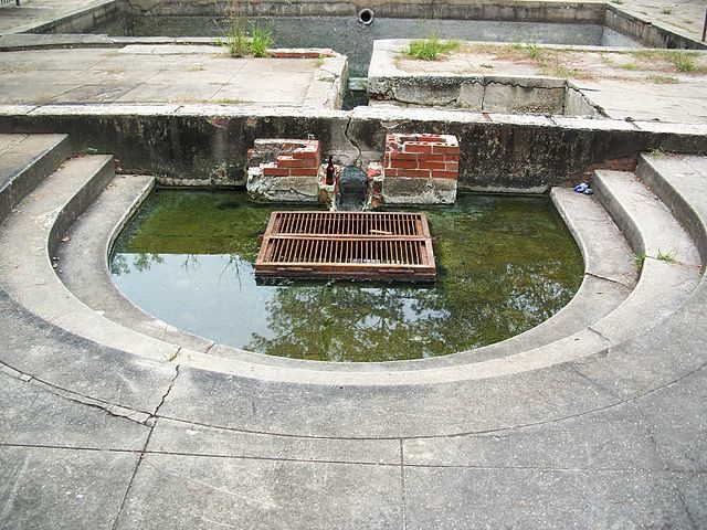 From beneath the grate in this picture the spring still bubbles up to fill the pool. The channel behind it (between the exposed brickwork) fills the second pool, and the overflow was directed into a nearby creek. Author: Ebyabe CC BY-SA 3.0