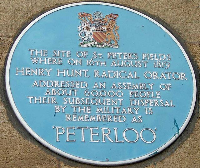 A blue plaque on the wall of the Free Trade Hall, commemorating the Peterloo Massacre on 16 August 1819. Author: Allan K Preston. CC BY-SA 3.0