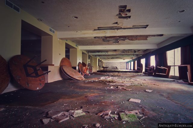 A large room with debris on the ground and round wooden tables up against the wall