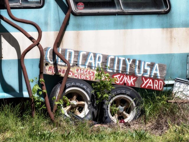 "Old Car City JUNK YARD" sign against a blue and white bus