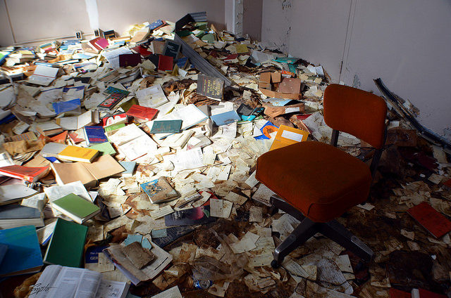 Books and papers strewn across the floor of a room, a chair at its center.