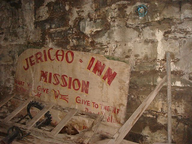 Sign that reads "JERICHO INN MISSION" leaned up against a brick wall