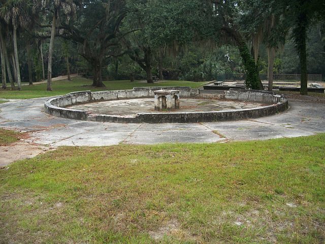 The remains of an ornamental pond, with one of the spa pools visible in the background on the right, and the bridge over Spring Creek to the left. Author: Ebyabe CC BY-SA 3.0