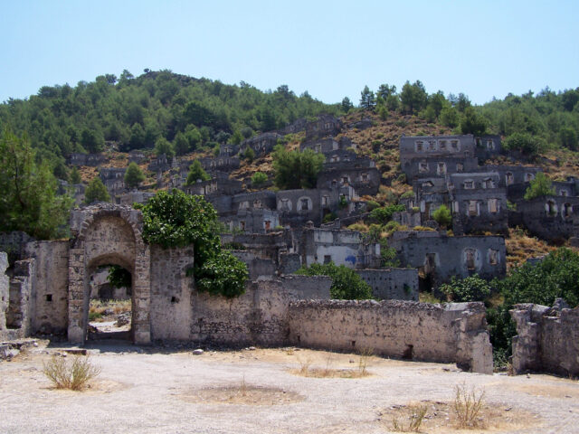 A stone gate with stone buildings nestled up a hill.