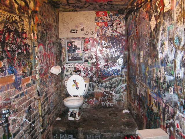 Washroom covered in graffiti, with a toilet in the corner