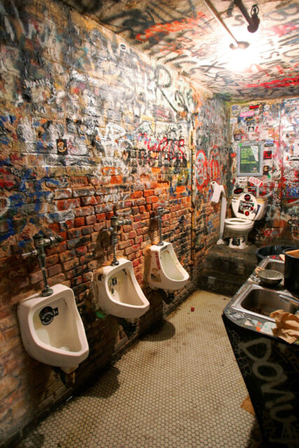 Urinals and a toilet along the walls of a graffiti-covered washroom
