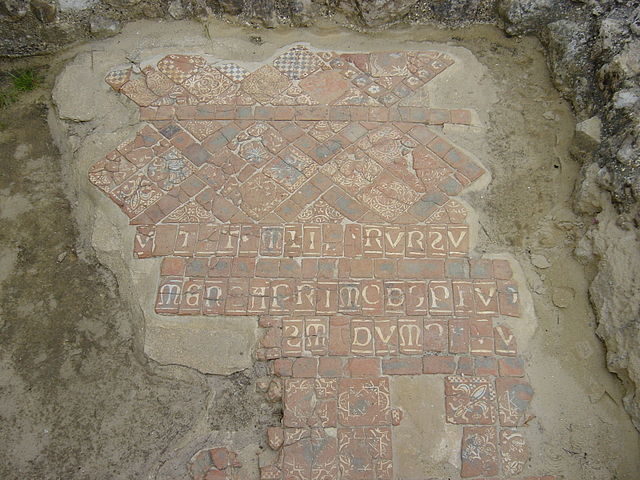 Medieval tiles placed in front of the door to the refectory. The Latin inscription says: “Before you sit down to eat your meal remember the poor.” Author: BenShade – CC BY-SA 3.0