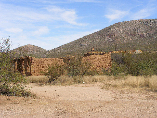 Roofless stone buildings surrounded by brush in the desert.