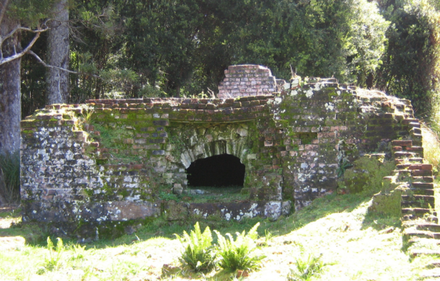 A stone wall covered in moss with a hole at its base.