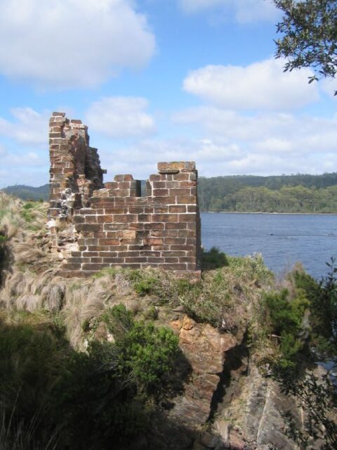 Partial remains of a stone wall on an island, water in the background.