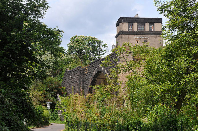 The overgrown ruins of the bridge. Author: Хрюша – CC BY-SA 3.0