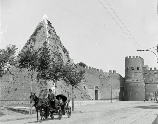 A man on a horse and carriage in front of a castle and pyramid.