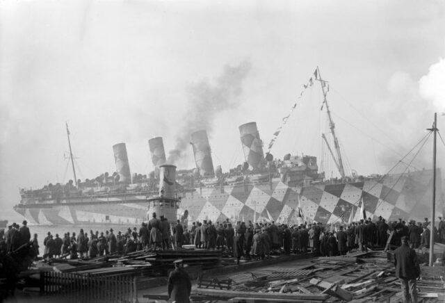 Troops standing around the HMS Tuberose, which is in dazzle camouflage