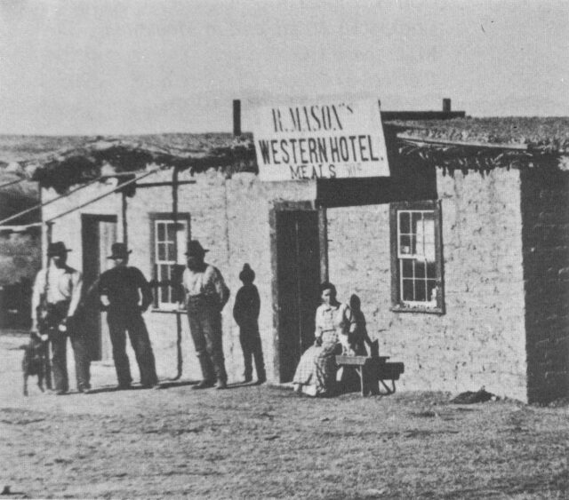 Three men and a woman positioned outside the front entrance of Mason's Western Hotel