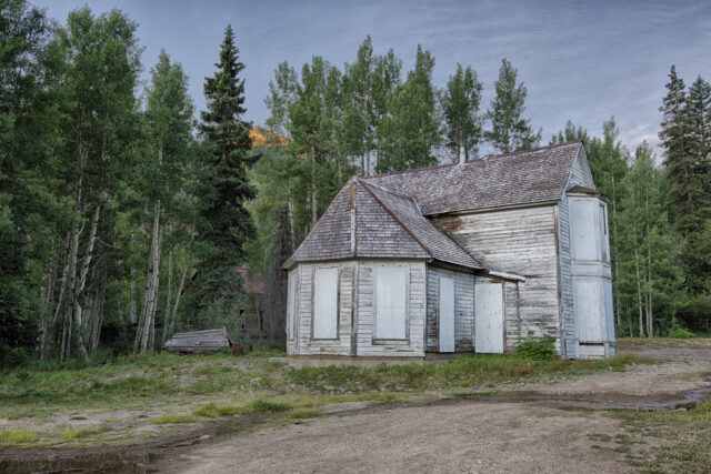 A white abandoned building sitting in a forest.
