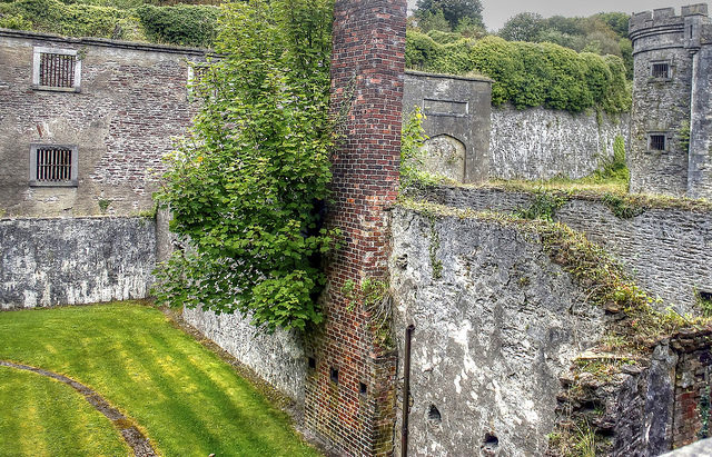 The harsh grays of the remains of the jail are tempered by the encroaching green of nature. Author: psyberartist CC BY 2.0