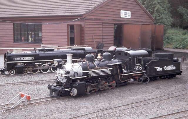 Miniature locomotives parked beside a building