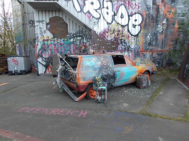 Damaged car parked outside of a graffiti-covered building