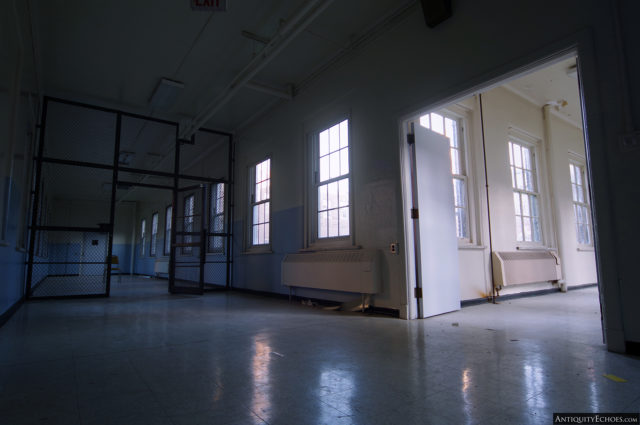 An L-shaped hallway, with a gated entrance on one side and a brightly-lit corridor on the other