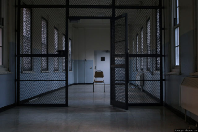 A chair placed in the middle of a hallway, just behind a gated entrance