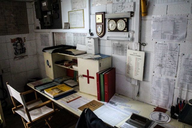 Papers and files lying on a desk that's up against a wall covered in more documents