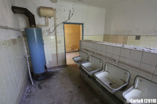 A room with a blue water heater on the left and a row of sinks on the right