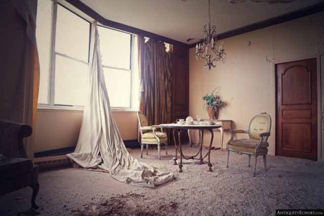 Abandoned room with a table, chairs and curtains hanging from the window