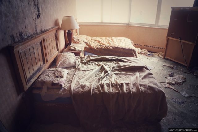 Two unmade beds separated by a bedside table and lamp