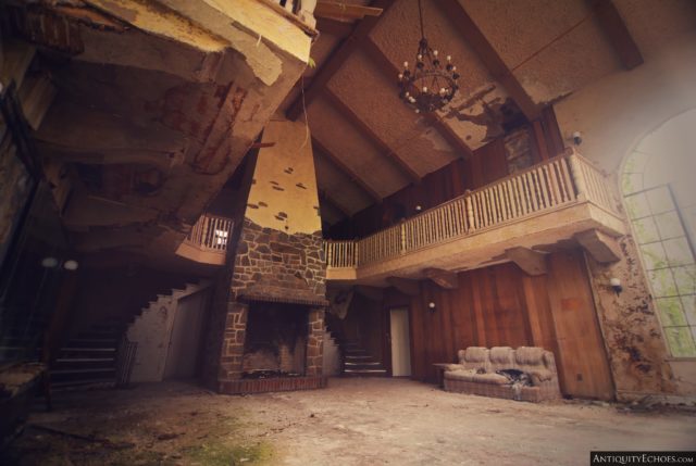 Large room with a couch against the wall, a fireplace at the center, a staircase and a chandelier on the ceiling