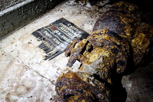 A rusty floor pipe with a piece of ripped, black paper beside it