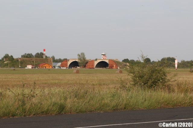 Grassy field with airplane hangars in the distance