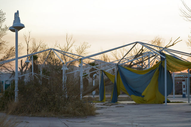 Metal roof beams covered in ripped yellow and blue tarp