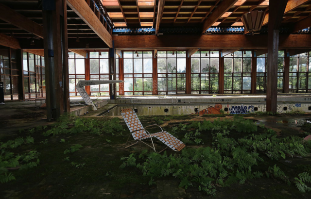 Pool chair in the middle of a moss-covered abandoned swimming pool complex