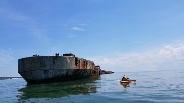 Kayaker paddling alongside a concrete ship