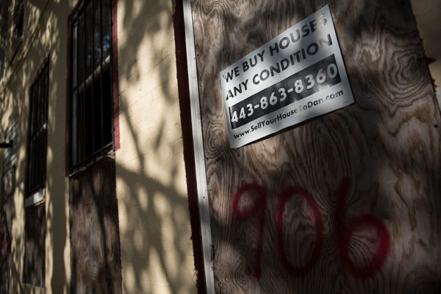 "WE BUY HOUSES ANY CONDITION" sign attached to a boarded up house