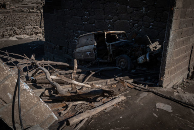 Rusty car parked beside a pile of tree branches