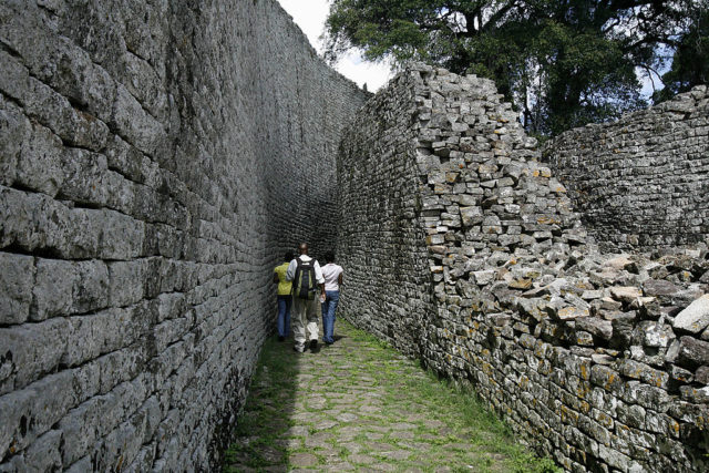 Tourists walk between the two large walls surrounding the ruins of Great Zimbabwe