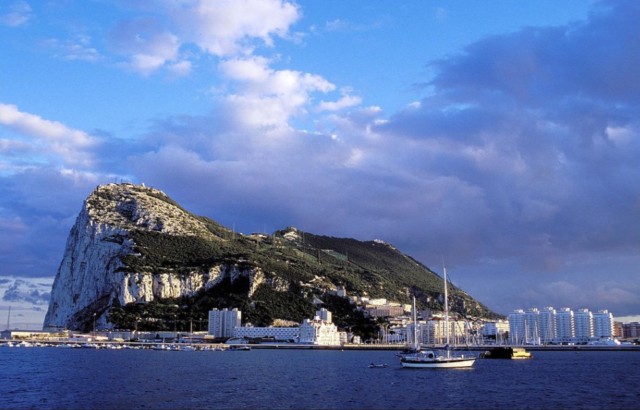 The Gibraltar Rock with a blue sky and clouds in the background, with water and boats in the foreground.