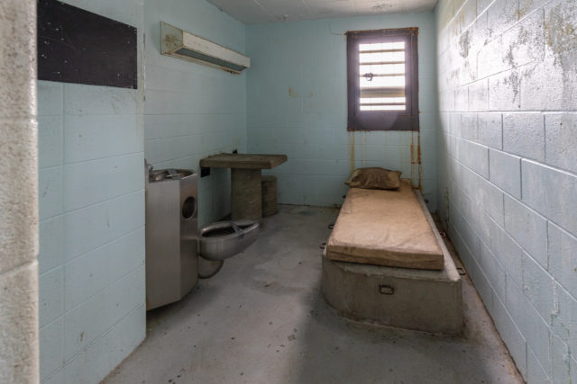 Interior of a prison cell, with a bed, desk and toilet