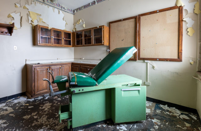 Doctor's office bed in a room with empty cabinets and paint peeling off the walls