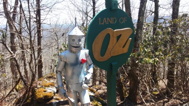 The tinman beside a sign that says the Land of Oz