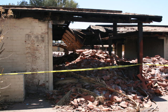 Side of a building with police tape and a large pile of destroyed red roof tiles. 