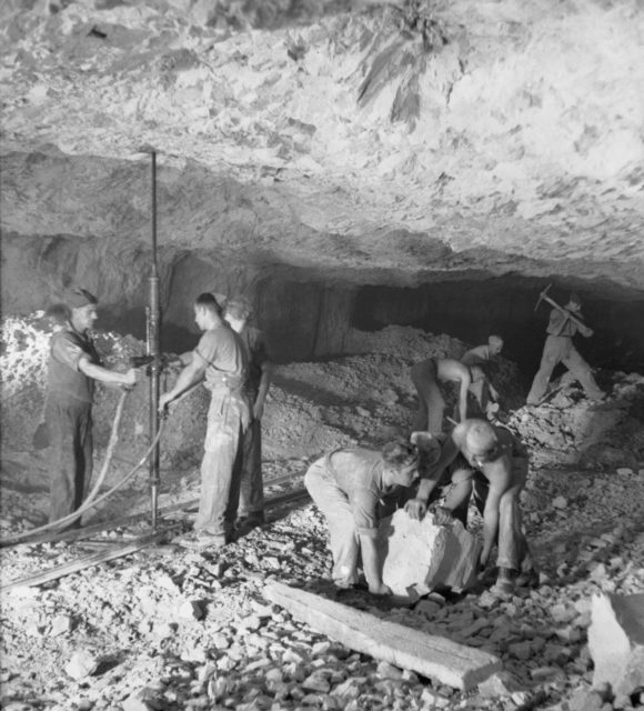 Group of Royal Engineers in uniform work on building a tunnel inside thick rock with low ceilings. 