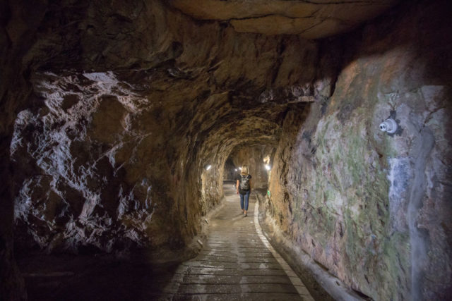 Woman walking down the middle of a tunnel with rock on either side.