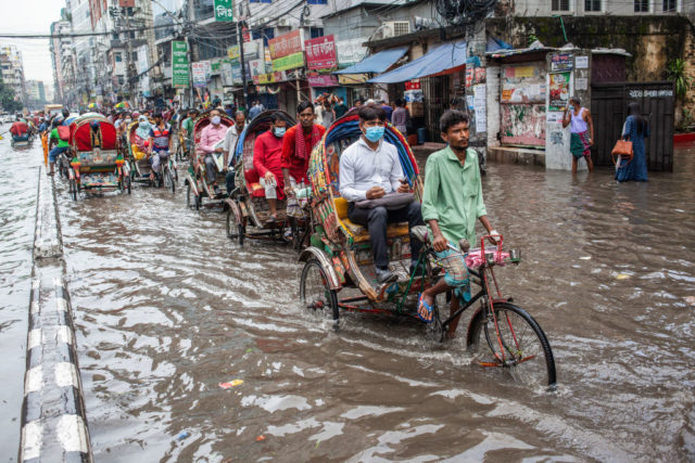People travel through a city street flooded with water on bikes 
