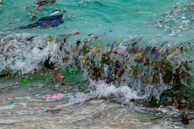 Wave full of garbage crashes on the shore.