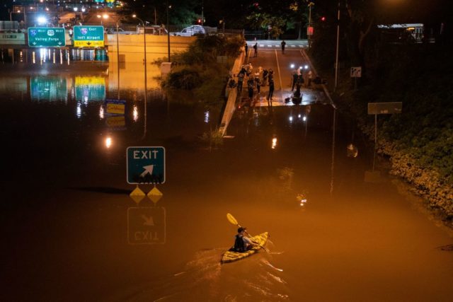 Man kayaking through a flooded city street.