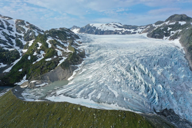 Glacier in the mountains with a green, grassy patch at the bottom.